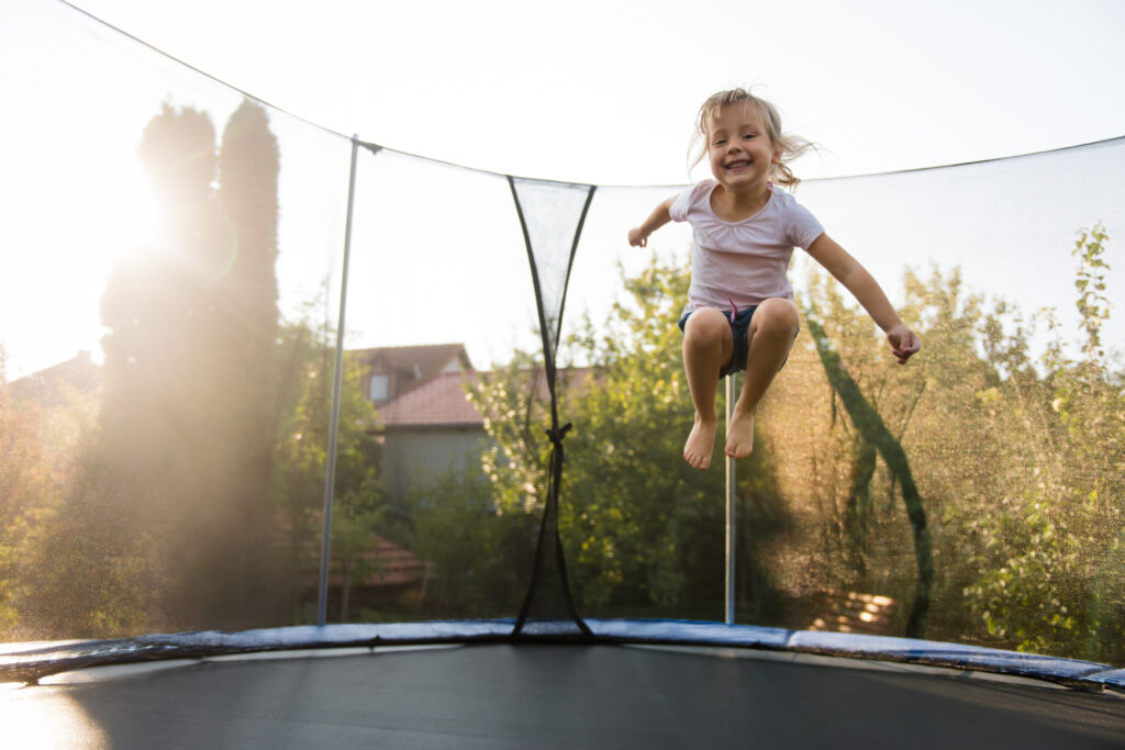 A young girl grins widely as she jumps on a trampoline.