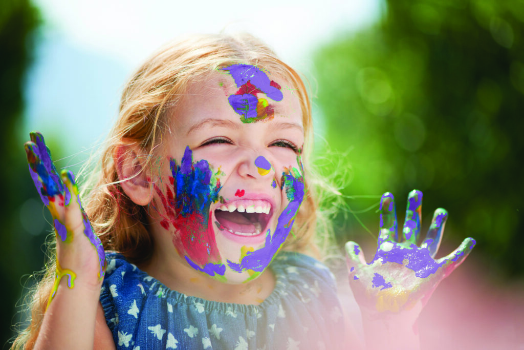 Little gleeful young girl with paint covering her hands face