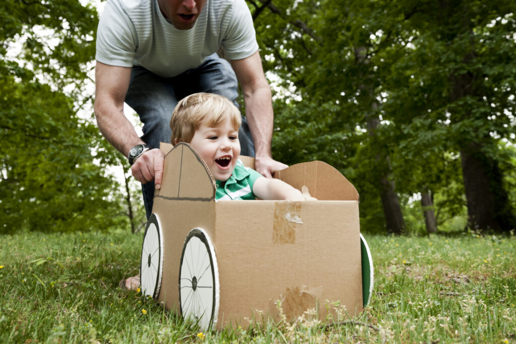 Father playing with his son riding in a recycled cardboard toy car