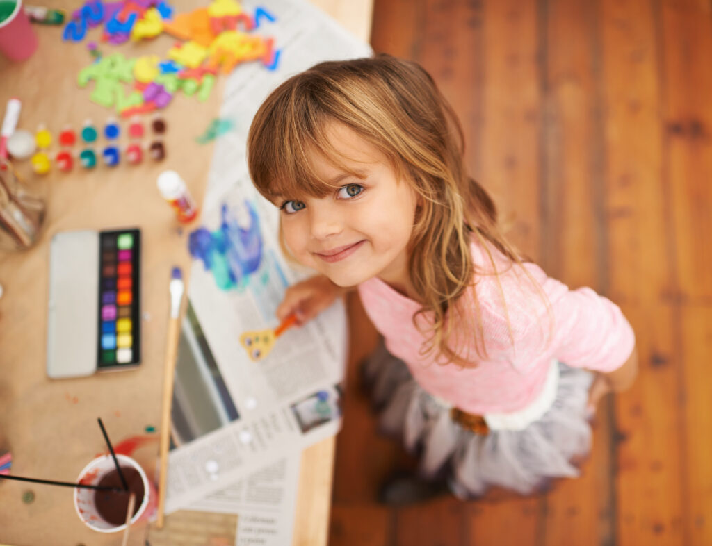 Young girl standing in front of a desk with art and colouring materials