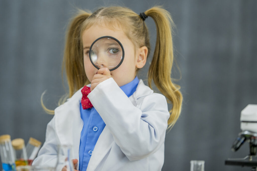A child dressed up in a lab gown looking through a magnifying glass