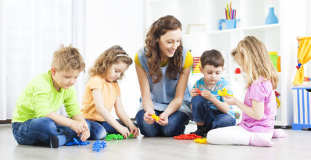 An educator playing with some toys with four toddlers.