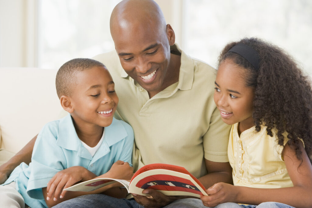 A smiling father reads a book with his young son and daugher