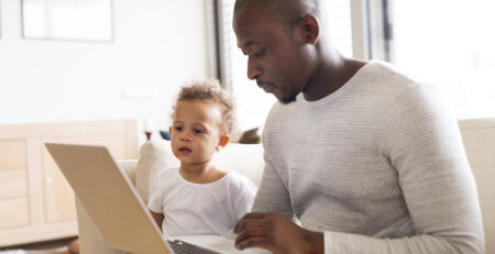 A father sitting beside his son as he looks they look at a laptop