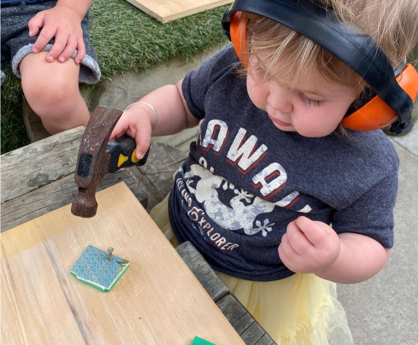 Young child wearing ear protection, hammering a nail