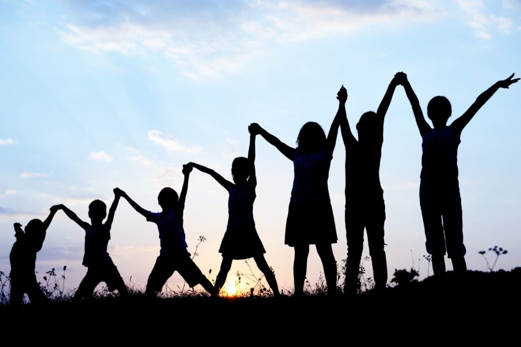 A silhouette of seven children standing with their arms raised, holding hands in a line 